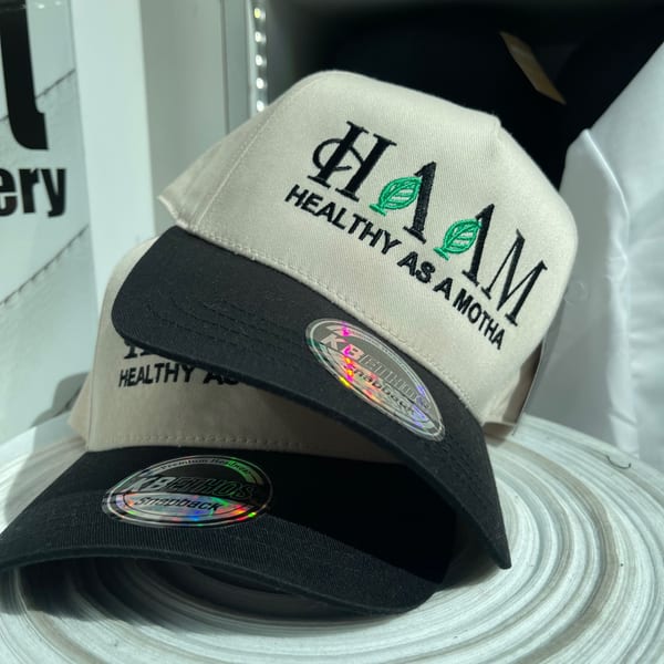 Two HAAM branded hats, beige with black brims, embroidered with "HEALTHY AS A MOTHA".