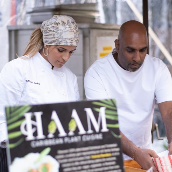 Two chefs, a woman and a man, working behind a HAAM Caribbean Plant Cuisine sign.