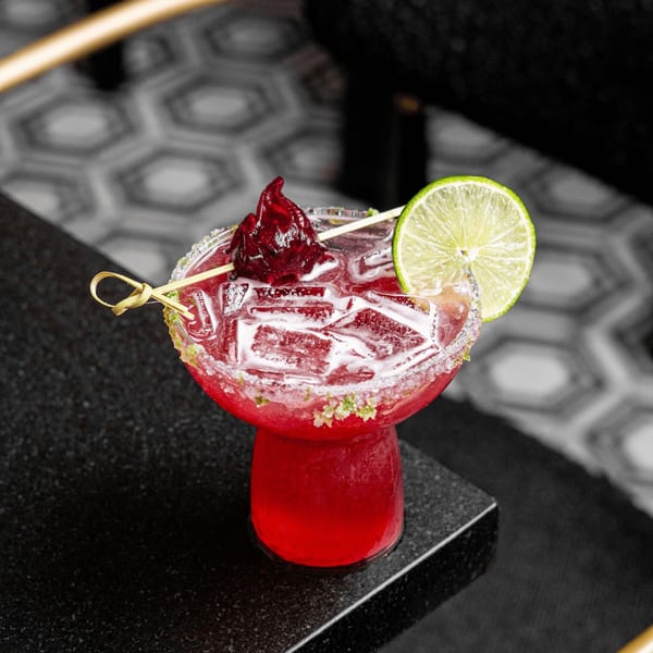 Vibrant red HAAM Caribbean Plant Cuisine cocktail with ice, lime, and hibiscus garnish on a dark surface.