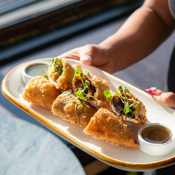 A server holds a plate of crispy vegan empanadas with microgreens and dipping sauces at HAAM.