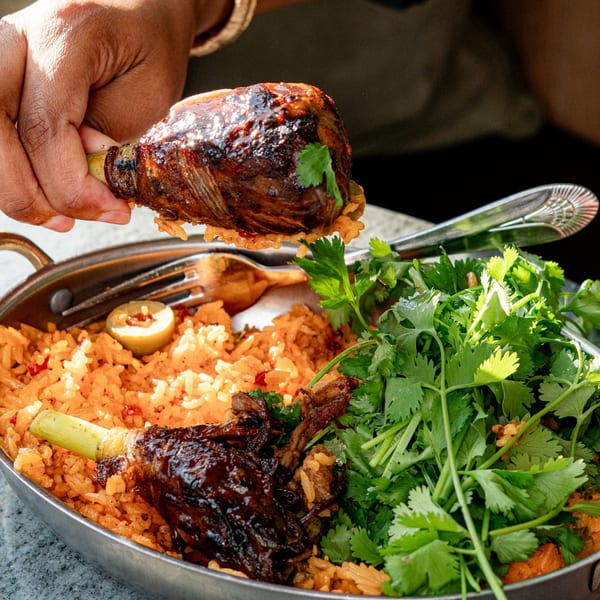 A hand holds a vegan HAAM Caribbean Plant Cuisine drumstick over a bowl of rice and cilantro.