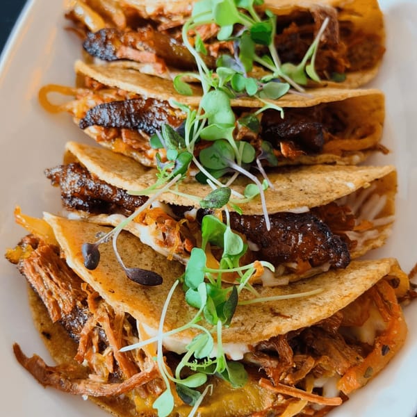 Four HAAM Caribbean Plant Cuisine vegan tacos with plant-based meat, cheese, and microgreens.
