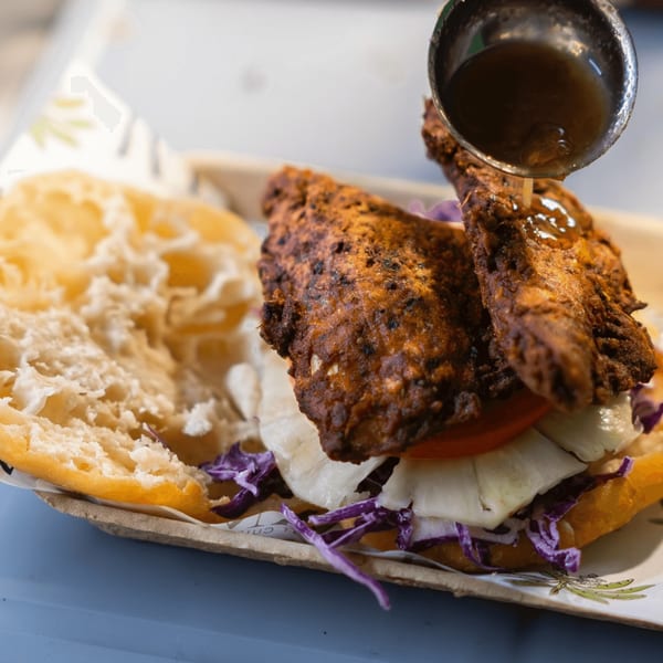 A vegan fried chicken sandwich with lettuce, tomato, and purple cabbage, drizzled with sauce.