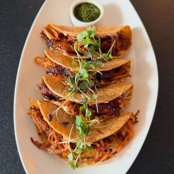 Five vegan tacos with plant-based meat, shredded vegetables, and microgreens, served with green sauce.