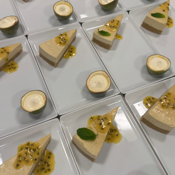 Vegan cheesecakes with passion fruit topping and halved passion fruits with cream on white plates.