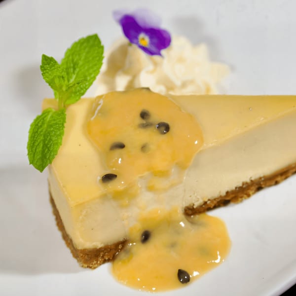 Vegan cheesecake slice with passion fruit topping, whipped cream, mint, and an edible flower.