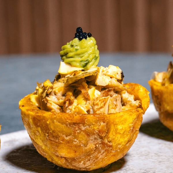 Close-up of a golden plantain cup filled with vegan meat, topped with green avocado cream and black caviar.